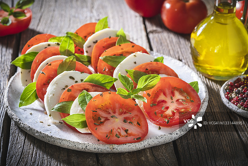 卡普雷塞沙拉：番茄、马苏里拉奶酪、牛至和橄榄油，乡村木桌图片素材