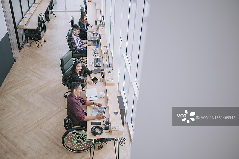 创意办公室中，坐在轮椅上的印度裔商人和他的中国女同事讨论工作（由上往下拍摄的高角度视图）图片素材