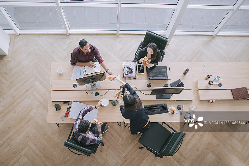 亚洲同事和印度同事在办公室工作站休息吃面包图片素材