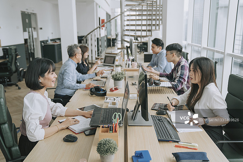 在开放式办公室里忙碌且愉快沟通的亚洲多种族白领图片素材
