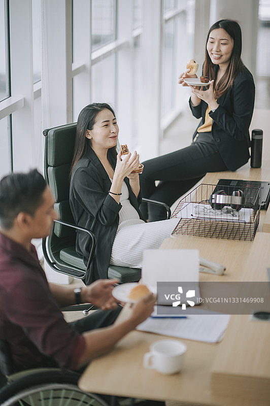 亚洲同事和印度同事在办公室工作站休息时分享面包零食的高角度视图图片素材