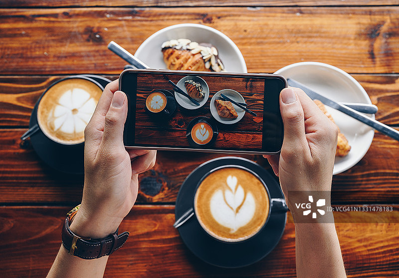 女人在咖啡馆用手机拍摄牛角包和牛奶咖啡图片素材