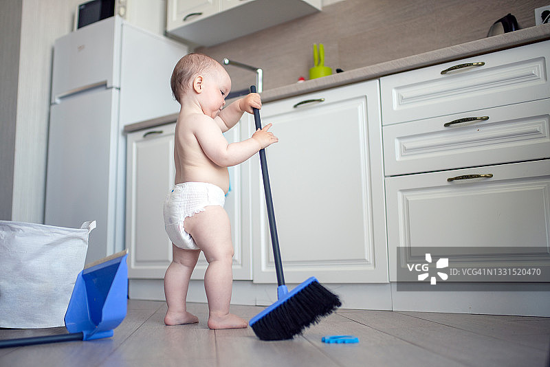 穿尿布的可爱男婴在厨房打扫地板图片素材