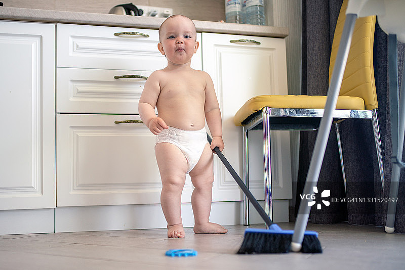 穿尿布的可爱男婴在厨房打扫地板图片素材