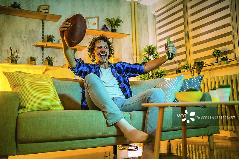 快乐的年轻男人在电视上看美式橄榄球比赛图片素材