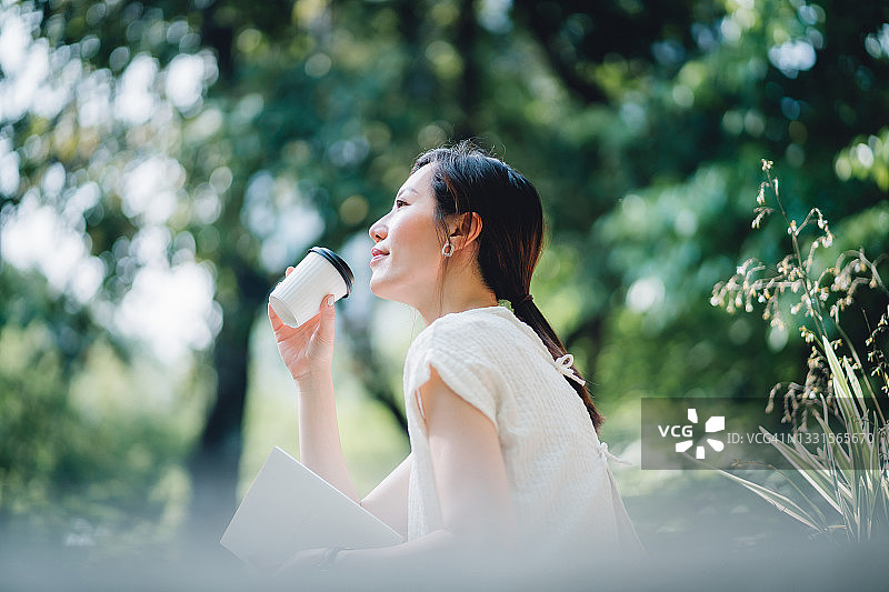 年轻的亚洲女性坐在公园长椅上，读书享受阳光图片素材