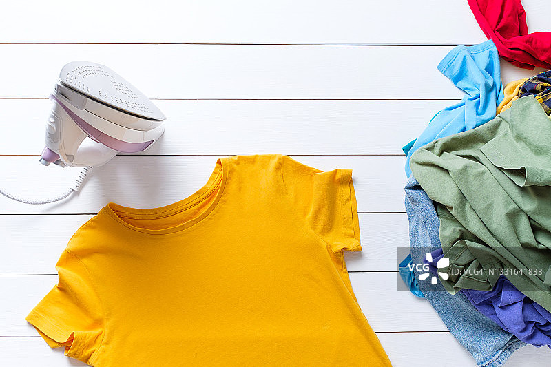 待熨烫的干净T恤或衣物，抽象背景。熨斗旁的家务概念图片素材