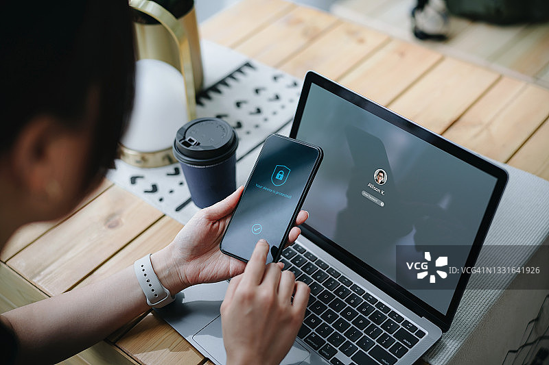 在办公桌上使用笔记本电脑并手持智能手机的年轻亚洲女商人图片素材