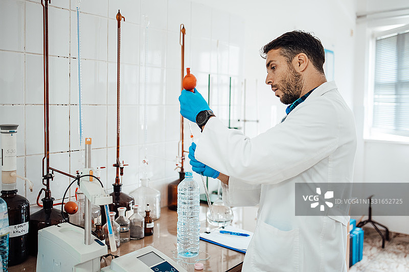 微笑的化学家在实验室里将水倒入试管中，水质检查概念图片素材