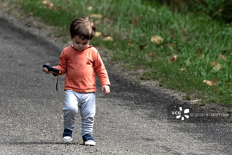 手持手电筒走在花园旁沥青路上的小男孩图片素材