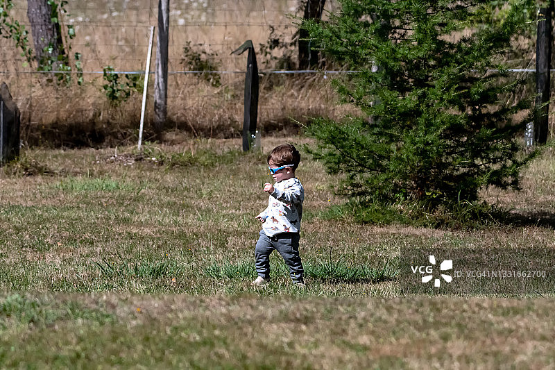 戴蓝色太阳镜在草地上行走的小男孩图片素材