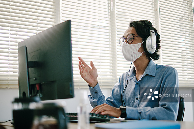 在办公室戴口罩，用电脑进行视频会议的年轻男人图片素材