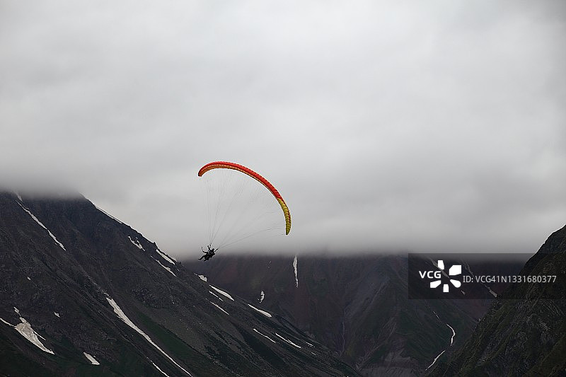 在多云天空下高加索山脉之间滑翔伞飞行图片素材