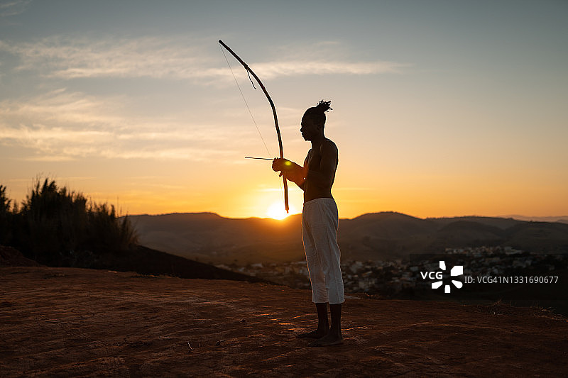 演奏贝林博乐器的卡波耶拉黑人男子，日落时分图片素材