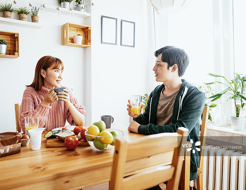 日本夫妇在家中厨房一起用餐，男人拿着橙汁微笑图片素材
