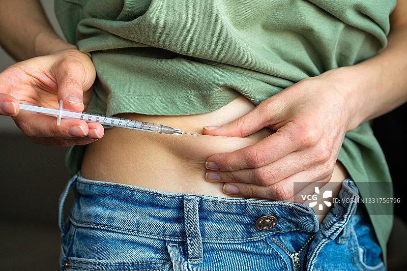 一位患有糖尿病的女人拉起腹部皮肤，用一次性注射器和小针头注射胰岛素，或者一位计划怀孕的女孩在人工授精或受孕前刺激排卵图片素材