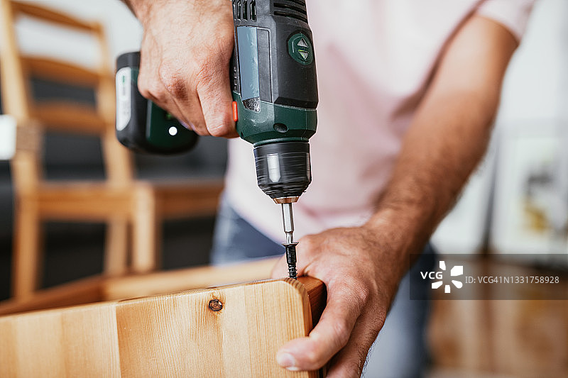 一位年长的男人在家做手工——将螺丝钻入新家具中图片素材