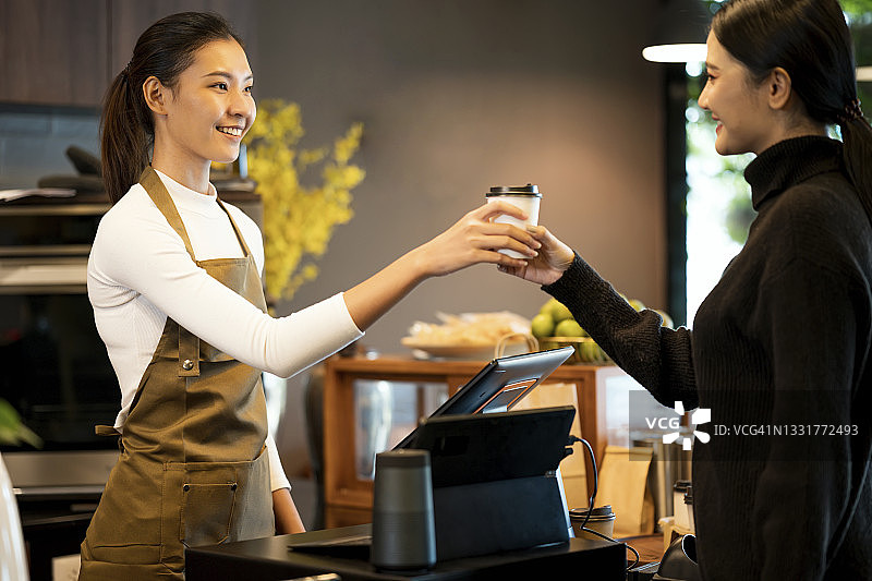 咖啡让我快乐。年轻亚洲女性咖啡店主在咖啡馆为顾客提供黑咖啡。用心服务，销售点系统和外卖食品。图片素材