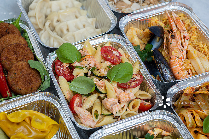 外卖：含健康天然中餐（饺子、鸡肉面条、鸡肉米饭、三文鱼意大利面、沙拉三明治）的不同铝制午餐盒。航空食品。飞机餐和小吃。外卖食品。图片素材