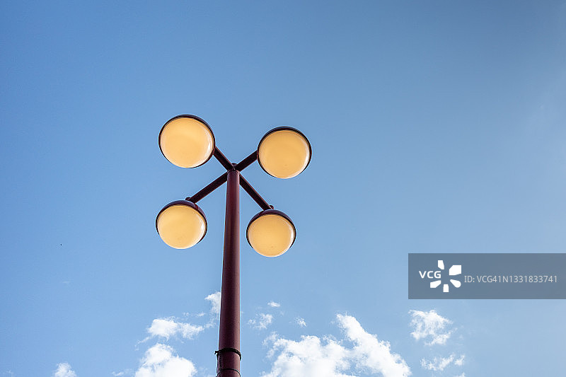 蓝天白云下球形黄色灯泡的复古红色街灯柱的仰视视角图片素材