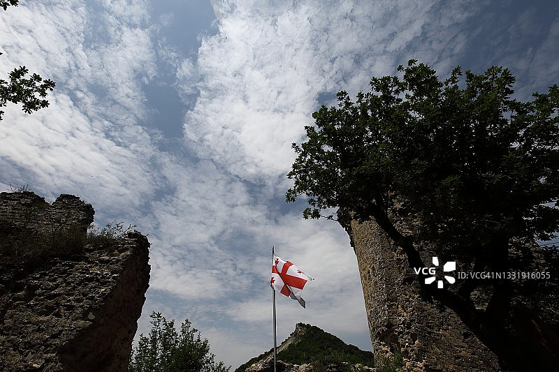 蓝色多云天空下古老城堡废墟间的格鲁吉亚国旗图片素材