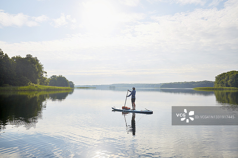 女人在田园诗般的湖面上划桨，夏日云朵和蓝天倒映在平静的水面上图片素材