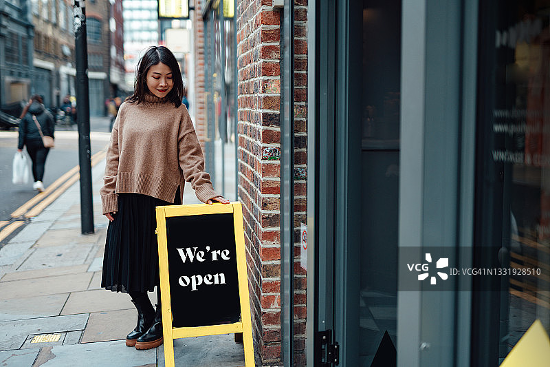 快乐的女店主站在商店招牌旁图片素材