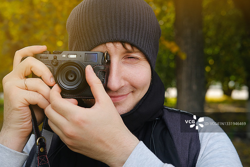 快乐开朗的年轻男人是摄影师、旅行者或在户外工作的游客。有创意的自由职业男性，休闲装和帽子的学生，用相机拍照。专业活动，爱好概念。图片素材