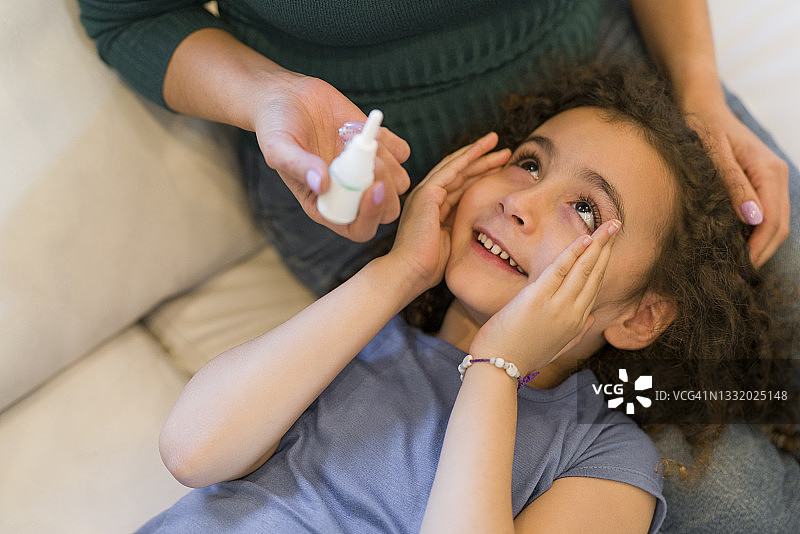 母亲在家中客厅给女儿滴眼药水图片素材