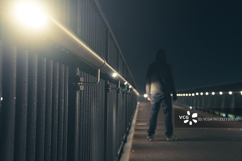 一个幽灵般的蒙面人，在夜晚的小路上的灯光下呈现剪影，具有景深编辑效果图片素材