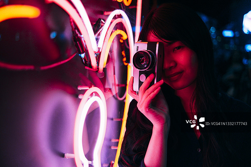 年轻女摄影师用复古相机拍摄霓虹灯图片素材