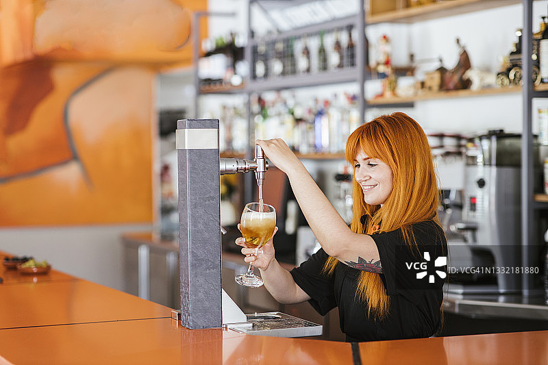 微笑的红发女服务员在酒吧用龙头接啤酒图片素材
