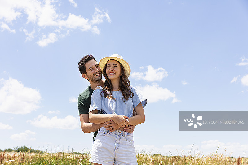 阳光明媚的日子里，笑容满面的男朋友站在女朋友身后图片素材