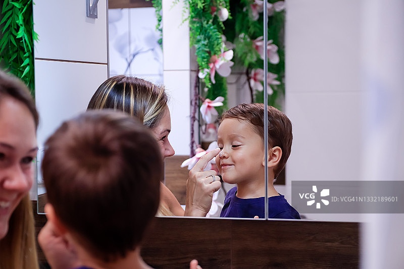 母亲给小儿子脸上涂润肤霜图片素材
