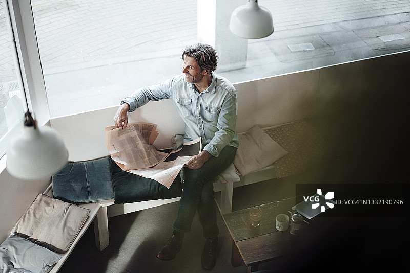 在咖啡馆玻璃窗边看报纸的微笑中年男人图片素材