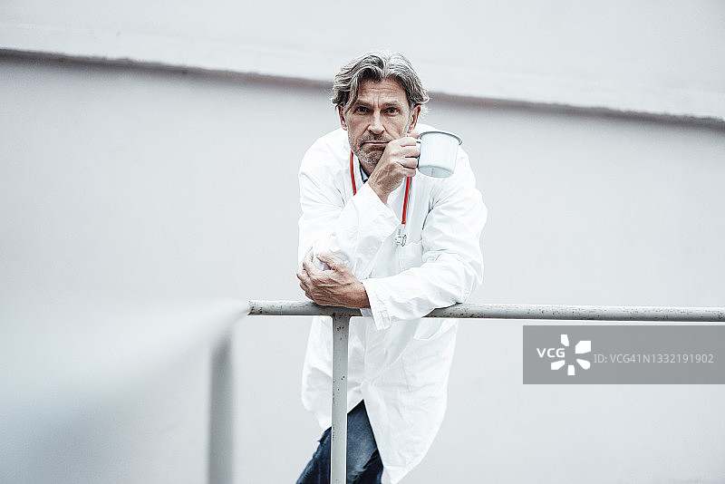 年长的男医生靠在栏杆上，拿着咖啡杯图片素材