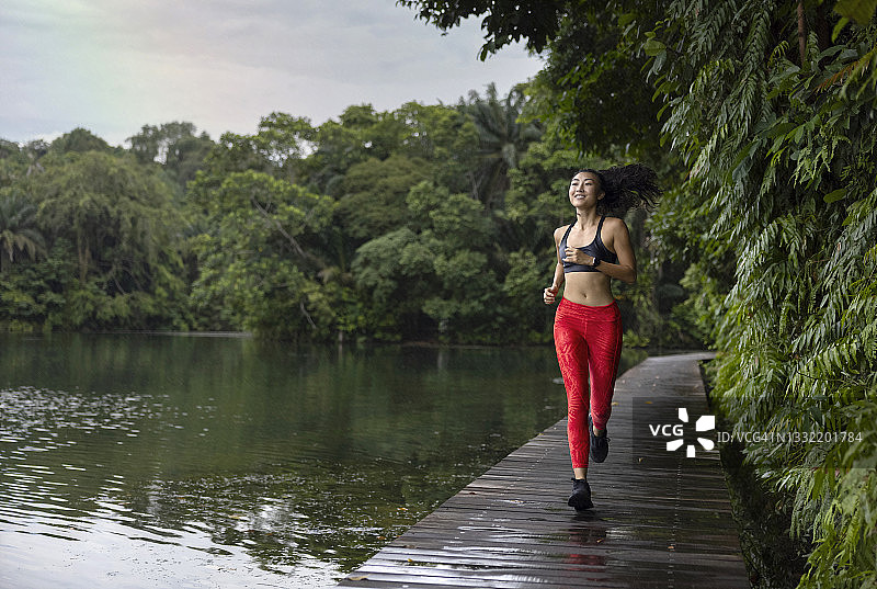 笑容满面的年轻女人在湖边木板路上跑步图片素材