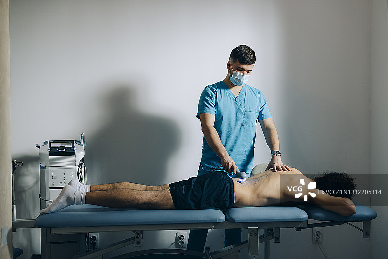 物理治疗：医生戴口罩使用激光治疗患者背部图片素材