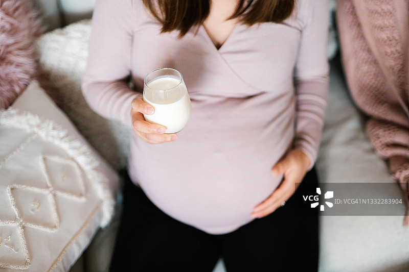 年轻孕妇在家中沙发上放松，喝一杯鲜牛奶俯视角度照片。健康饮食，健康怀孕生活方式图片素材