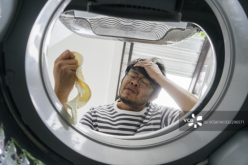 洗衣机内部的低角度视图：亚裔单身父亲对婴儿围裙脏了，需要经常清洗感到担忧和无聊图片素材
