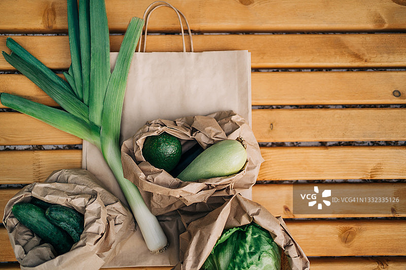 绿色蔬菜：牛皮纸袋中的韭葱，旁边是鳄梨、蔬菜瓜、黄瓜和卷心菜，环保配送理念设计样机图片素材
