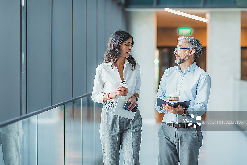 微笑的商务人士走在现代化的办公室大厅或走廊上，快乐的同事聊天，一起去会议室开会或简报，合作概念图片素材