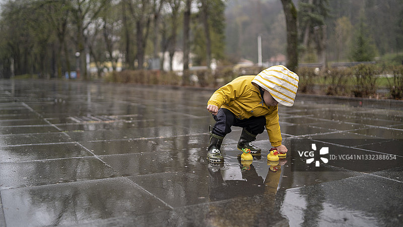可爱的宝宝穿着黄色雨衣和雨靴在雨天玩鸭子图片素材