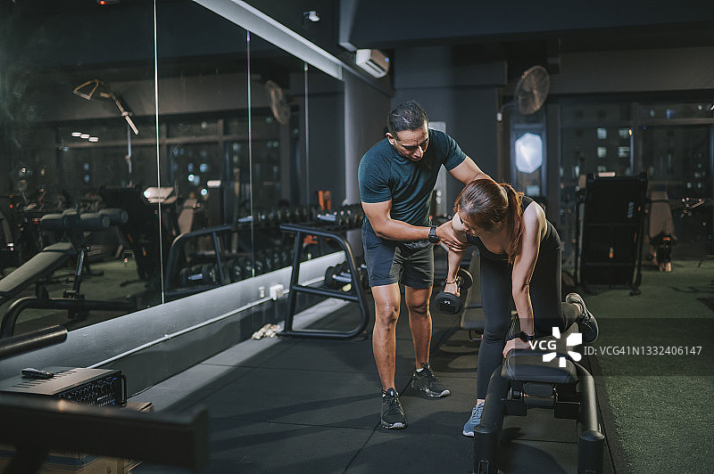 健身教练指导亚洲中年妇女在健身房的卧推凳上用哑铃做弓步图片素材