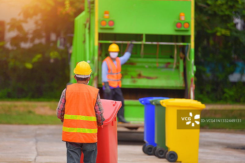 两名清洁工站在垃圾车旁倾倒垃圾箱，泰国图片素材