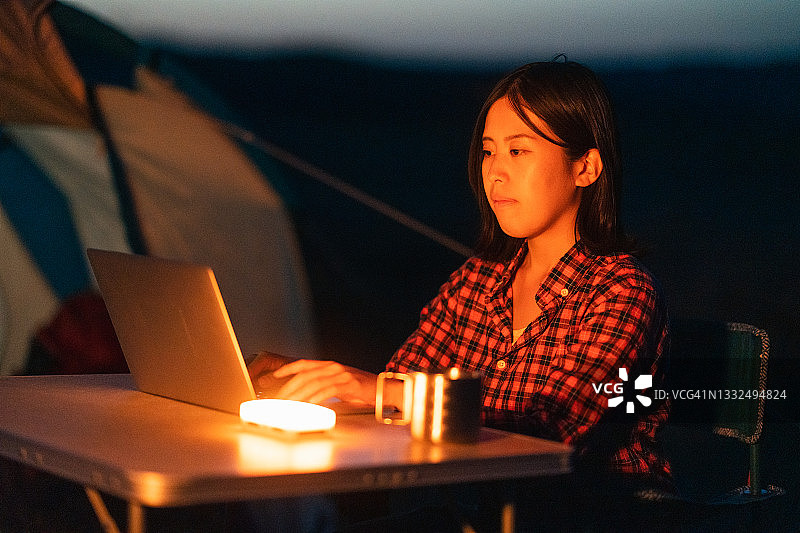 年轻女人在野外露营时在帐篷旁使用笔记本电脑图片素材