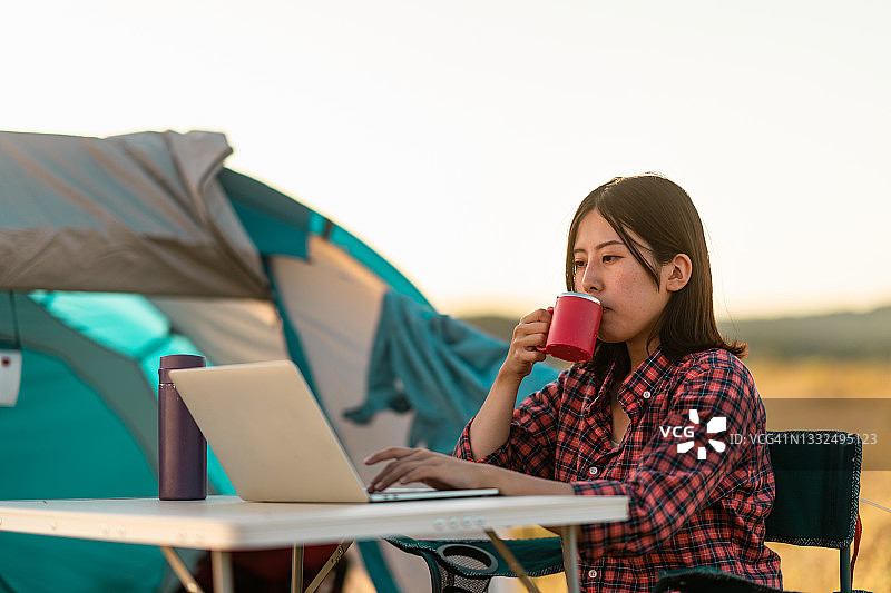 年轻女人在野外露营时在帐篷旁使用笔记本电脑图片素材