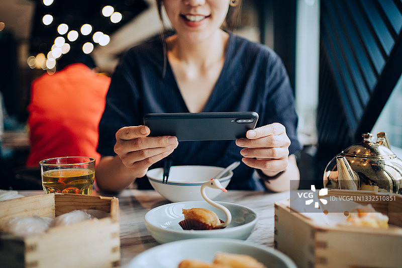 年轻女子在餐厅用手机拍摄美味的中国点心图片素材