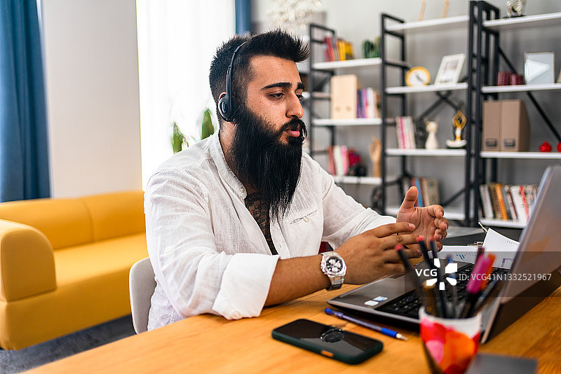 在家工作的时尚文化自由职业者，坐在笔记本电脑前的工作桌旁，看着笔记本电脑图片素材
