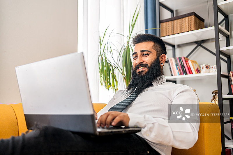 在家工作的时尚自由职业者，坐在沙发上看着笔记本电脑图片素材